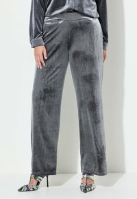 Graue Samt-Hosen mit weitem Bein, die eine glatte Textur und einen elastischen Bund haben, kombiniert mit mehrfarbigen, geschnürten High Heels.
