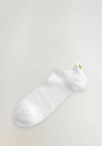Vit bomullssocka med en slät textur, med en gul broderad design nära vristen. Ankel-längd, enkel och minimalistisk design.
