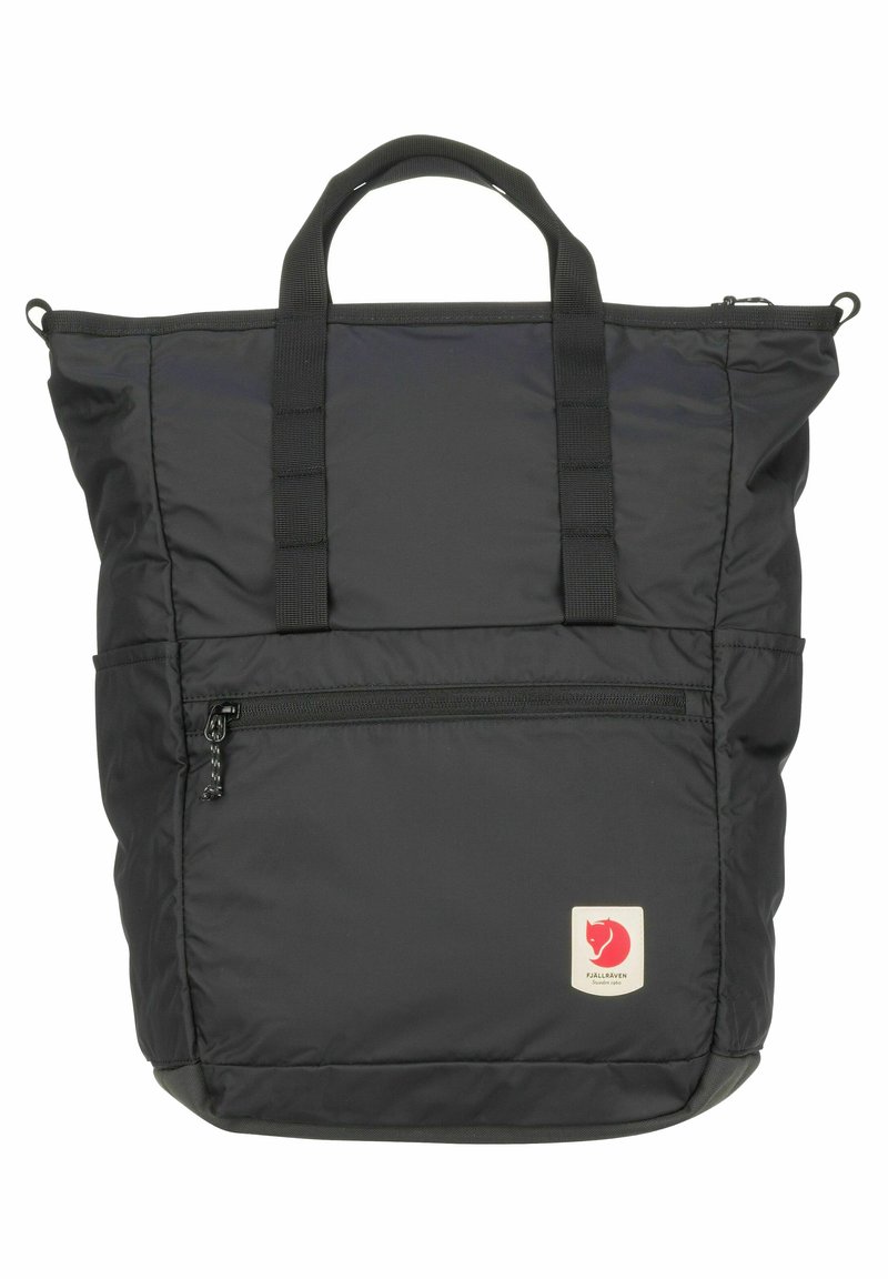 Sac en nylon noir avec poignées supérieures doubles, poche avant zippée et patch logo. Possède une texture douce et une forme rectangulaire.