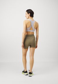 Grå sports-bh med utskåret ryggdetalj, kombinert med olivgrønne shorts med svart logo-linning, og svarte joggesko med grønne detaljer.