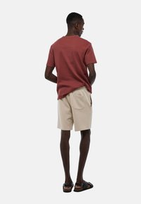 T-shirt rouge à manches courtes et côtelé, associé à un short beige avec une poche à l'arrière. Porté avec des sandales noires, mettant en avant une coupe décontractée.