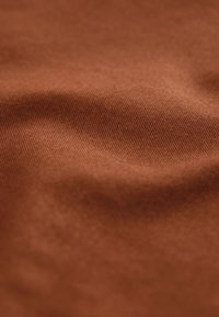 Tela de algodón marrón con una textura suave, que muestra arrugas sutiles y un patrón de tejido uniforme en toda la superficie.