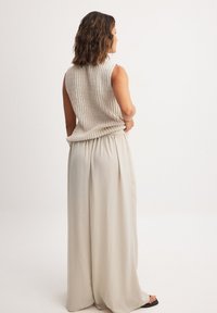 Débardeur tricoté sans manches de couleur beige clair avec une finition texturée, associé à une jupe fluide crème ; tissu doux avec une taille froncée.