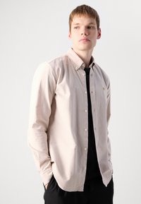Šviesiai smėlio spalvos marškiniai su mygtukais, pagaminti iš minkštos medžiagos. Turi ilgomis rankovėmis, apykaklę ir mažą logotipą ant krūtinės.