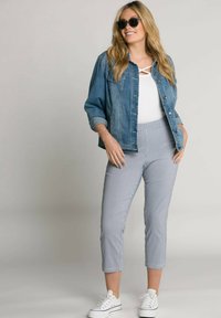 Denim jas, witte top met kruisdetail, blauw-wit geruite cropped broek en witte sneakers. Zwarte zonnebril maakt de look compleet.
