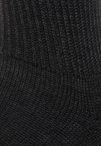 Chaussette noire en tricot avec texture côtelée et coutures lisses et régulières. Présente une sensation douce et un revers élastique pour un ajustement sécurisé.