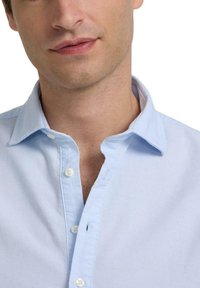 Camisa de botones azul claro con un cuello clásico, que presenta una textura suave y un solo botón visible cerca de la apertura del cuello.