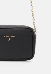 Bolso cruzado de cuero negro con forma rectangular, correa de cadena dorada y logo de la marca en relieve en la parte frontal. Detalle de cierre con cremallera.