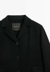 Manteau en laine noir à boutons, col cranté et poches avant, étiquette indiquant la marque Massimo Dutti.