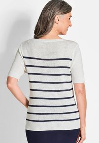 Korte mouwen gestreepte trui van witte garen met marineblauwe horizontale strepen. Heeft een wijde halslijn en een geribde zoom. Gelaagd gebreid stof.