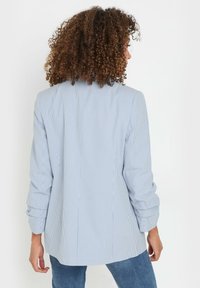 Randig skjorta i ljusblått och vitt, tillverkad av mjukt tyg. Har långa ärmar och en avslappnad passform med en något rundad nederkant.