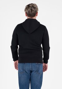 Felpa nera con cappuccio, dal design aderente, maniche lunghe e una texture morbida, abbinata a jeans in denim blu.