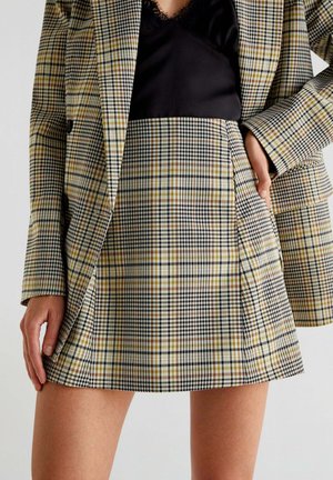 Geruite rok in geel, zwart en bruin, met een uitlopende vorm en plooien. Het combineren met een zwarte top creëert een gelaagde look.