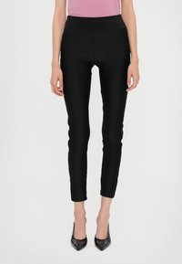 Leggings neri aderenti con una texture liscia, vita alta e design alla caviglia, abbinati a tacchi neri lucidi.