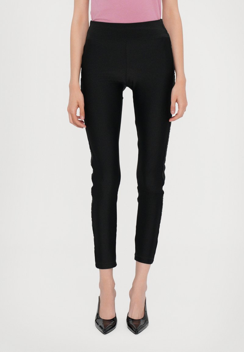 Leggings neri aderenti con una texture liscia, vita alta e design alla caviglia, abbinati a tacchi neri lucidi.