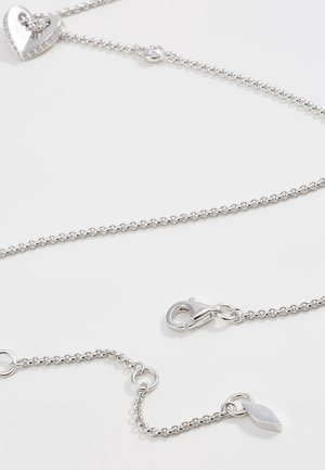 Zilveren ketting met lobster sluiting, kleine ronde schakels, hartvormige hanger met ingelegde stenen en merklabel detail.