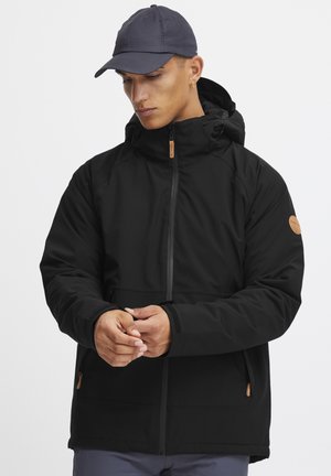 Black hooded jacket featuring a front zipper, elastic cuffs, and a tan leather accent on the sleeve. Smooth texture with a relaxed fit.