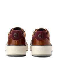 Hnědé kožené tenisky s vínovými akcenty z semiše, bílé podrážky a logo na patě. Vyznačují se kontrastním prošíváním a hladkými texturami.