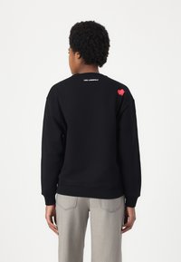 Sweatshirt preto em mistura de algodão, apresentando um detalhe de coração vermelho nas costas e um logo branco na gola. Mangas longas, punhos canelados.