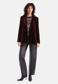 Bordeauxfarbenes Samt-Doppelbreasted-Blazer mit Revers, getragen über einem gestreiften Stricktop, kombiniert mit hoch taillierten grauen Jeans und schwarzen Pumps.