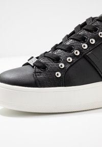 Mustat lenkkarit, joissa on monimateriaalinen muotoilu, tekstuuriset sivut, metallinapit ja valkoinen kumipohja. Nauhat ovat mustat hopeakorostuksilla.