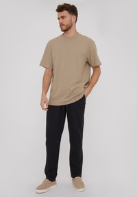 Camisa corta de manga corta en tono beige con textura, combinada con pantalones sueltos negros y calzado de color claro, presentando un ajuste relajado y un cuello redondo.