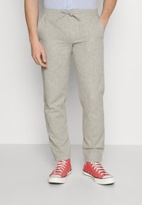 Ljust beige byxor i en texturerad tygkvalitet, med elastisk midja och dragsko. Matchas med röda högklackade sneakers.