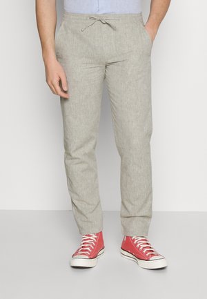 Helle beige Hose aus strukturiertem Stoff, mit elastischem Bund und Kordelzug. Kombiniert mit roten High-Top-Sneakern.