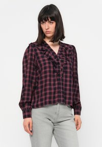 Long-sleeve blouse in dark blue and red plaid, featuring a ruffled neckline and front button closure, made from lightweight fabric.