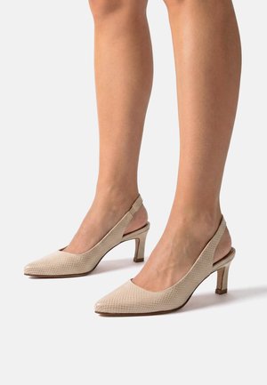 Nogi w beżowych, teksturowanych czółenkach typu slingback na wysokim obcasie, z ostro zakończonymi noskami i wąskimi, średniej wysokości obcasami na neutralnym tle.