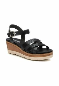 Sandalias de cuña negras con correas de cuero perforadas, correa ajustable en el tobillo y una suela de plataforma marrón claro con detalles texturizados.