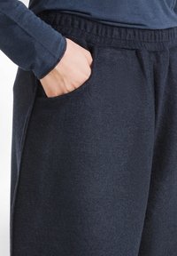 Donkerblauwe sweatpants van zacht materiaal, met een zijzak en een elastische tailleband voor comfort. Soepele textuur en een ontspannen pasvorm.