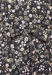 Zwarte stof met een klein roze, witte en gele bloemenpatroon, gestrikt aan de taille in een strik.