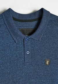 Granatowa koszulka polo z teksturowanej tkaniny, z kołnierzykiem na dwa guziki i małym haftowanym logo po lewej stronie klatki piersiowej. Miękki i swobodny design.