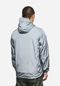 Giacca leggera con cappuccio in morbido grigio tenue con texture ripstop. Presenta polsini elastici e una vestibilità rilassata per il massimo comfort.