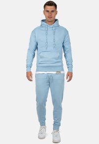 Felpa leggera azzurra e pantaloni jogger coordinati, realizzati in tessuto morbido, con tasca frontale, coulisse e polsini elasticizzati. Accentuato da un'etichetta.