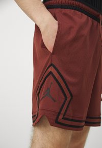 Pantalones cortos deportivos rojos con una tela de malla transpirable, ribetes negros y un destacado logo negro de Jumpman en el dobladillo inferior.