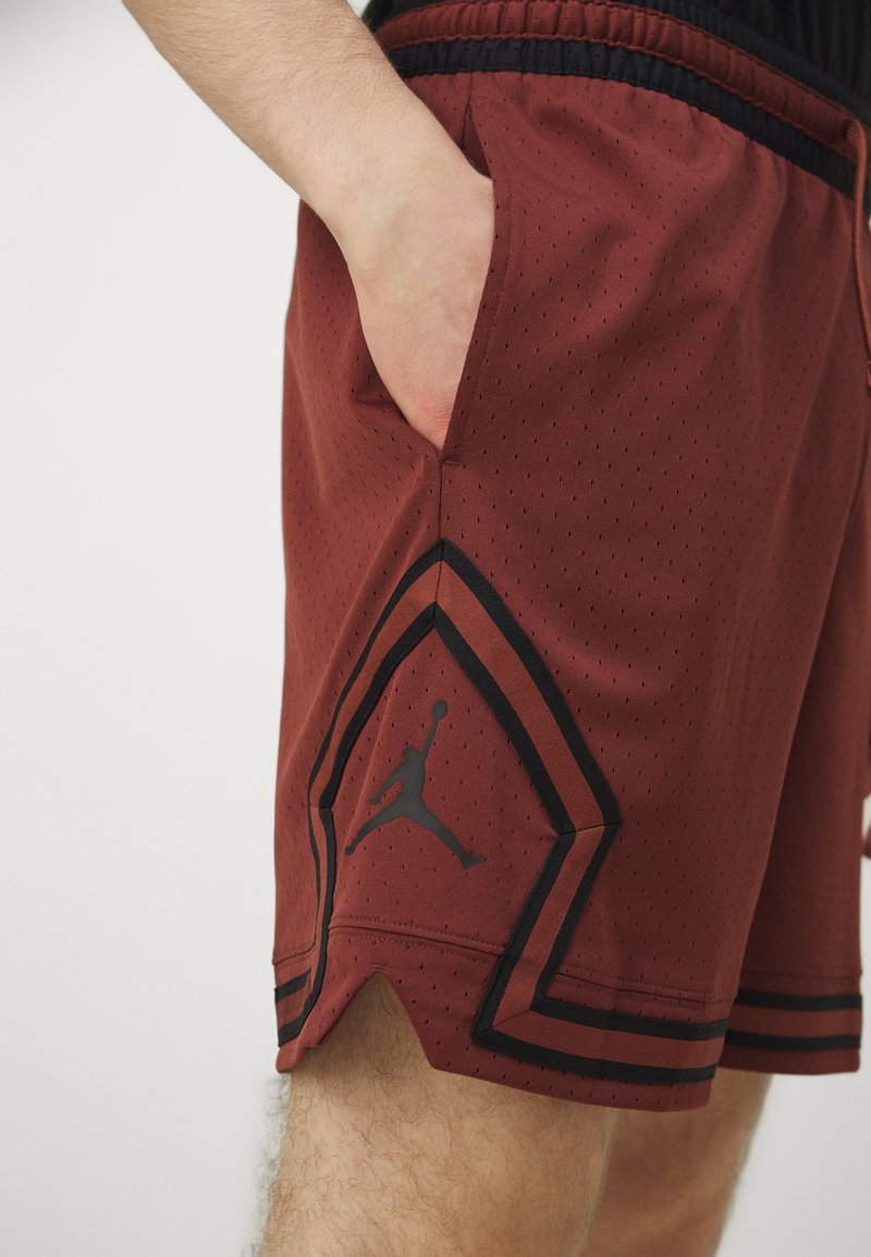 Czerwone szorty sportowe z oddychającej siateczki, z czarnymi wykończeniami oraz wyraźnym czarnym logo Jumpman na dolnym obszyciu.