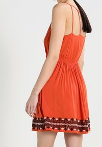 Robe sans manches orange avec une taille cintrée et un motif floral noir brodé à l'ourlet. Tissu léger et coupe décontractée.