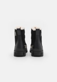 Sorte semskede ankelstøvler med ullfor, utstyrt med en robust gummisåle og bakre pull-tab. Enkel design med Sorel-merket på hælen.
