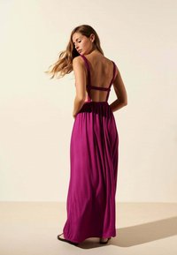Robe longue et fluide de couleur violette éclatante, dotée de fines bretelles, d'un dos nu et d'une taille froncée. Fabriquée en tissu doux avec une texture lisse.
