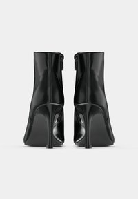 Botas de tornozelo de salto alto em couro preto com acabamento brilhante, fecho com zíper na parte de trás e design com ponta afilada. Textura suave e silhueta elegante.