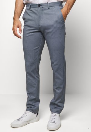 Pantaloni a righe blu chiaro con un design slim fit, dotati di tasche frontali, chiusura a un pulsante e sneakers bianche.
