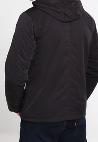 Czarna pikowana kurtka z kapturem, o gładkiej teksturze, przeszywanym wzorze i elastycznych mankietach. Prosty, funkcjonalny styl idealny na zimne dni.