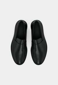 Fekete bőr slip-on cipők lekerekített orral, sima textúrával és minimalista dizájnnal. Elöl pánttal és lapos talppal rendelkeznek.