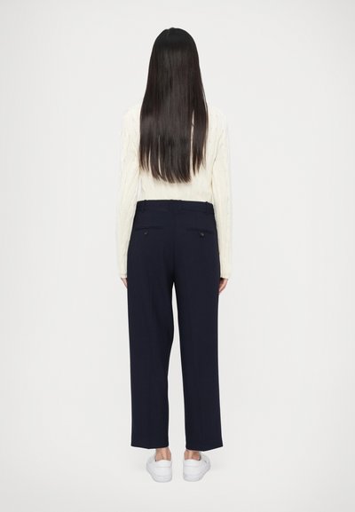 Mornarsko modre hlače s ravnim krojem, z zadnjimi žepi in gladko teksturo, kombinirane s kremnim puloverjem z vzorcem kit.