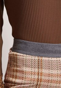 Ribbed brown bodysuit paired with patterned pink and orange zigzag pants, featuring a textured gray waistband and detailed stitching.