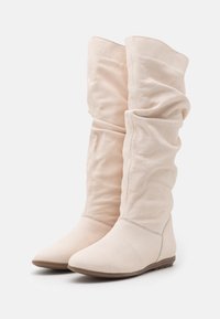 Botas caña baja, holgadas, hechas de piel suave de color crema con una textura lisa y suela plana. Presentan un diseño de punta afilada.