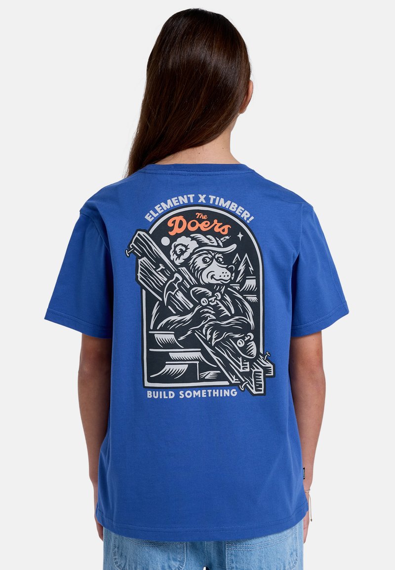 Camiseta de algodón azul con un gráfico de un oso sosteniendo herramientas, con el texto "Constrúyelo" abajo; de manga corta y diseño de cuello clásico.