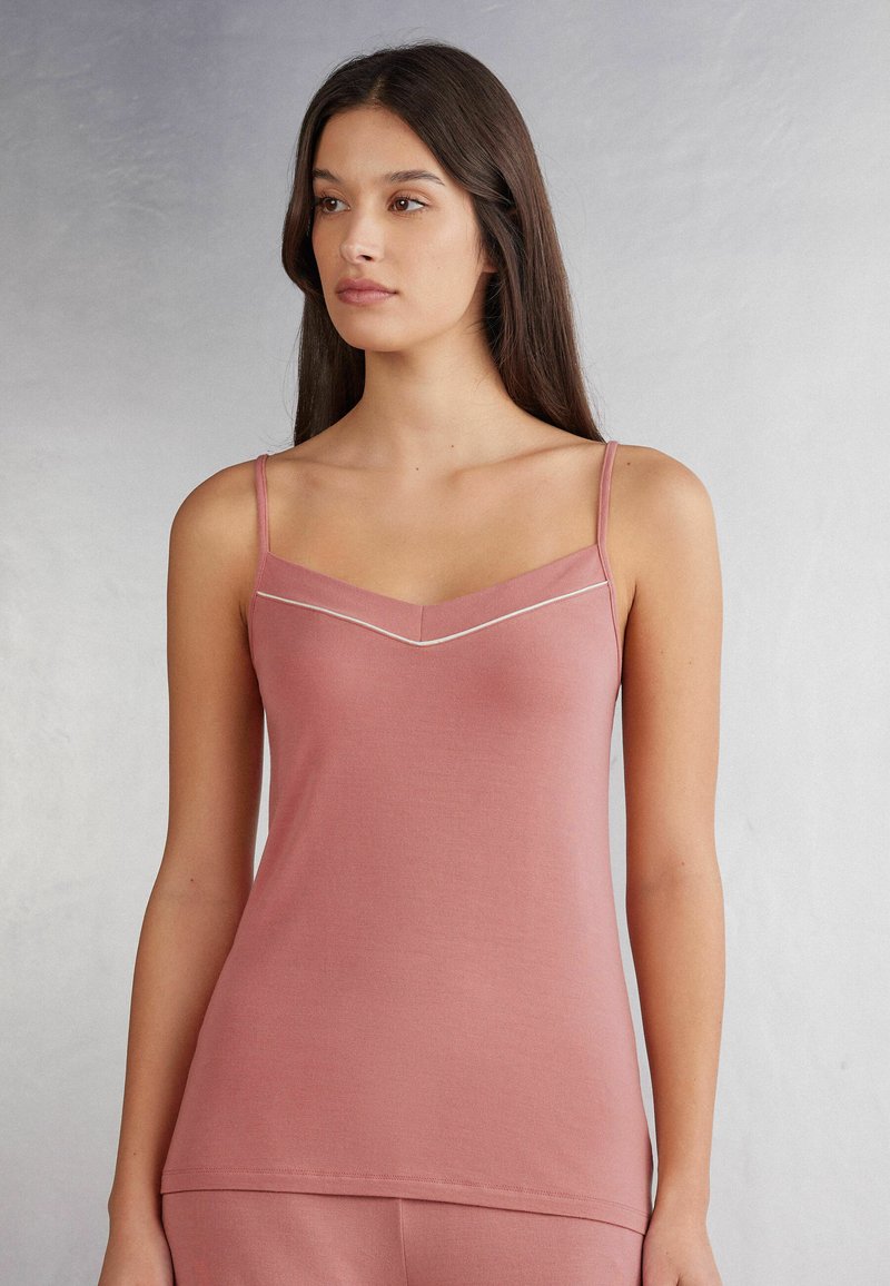 Różowy top na ramiączkach z gładkiego materiału, z cienkimi ramiączkami i subtelnym dekoltem w kształcie litery V, ozdobiony kontrastowym wykończeniem dla dodatkowego efektu.